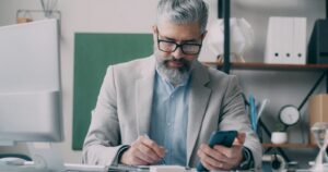 A man sitting at a desk using a cell phone